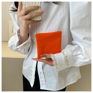 Close-up of a model holding a mini orange leather pouch against a white lace shirt