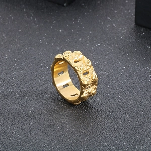 Detailed close-up of a wide golden punk skull ring with embossed texture on gray background