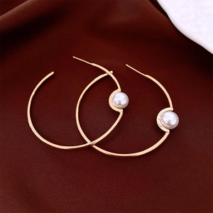 Macro detail of gold-plated hoop earring featuring a white pearl on deep velvet