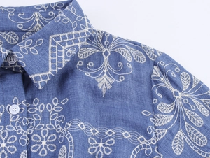 Détails de broderie florale blanche sur une robe chemise bleue en texture denim fine