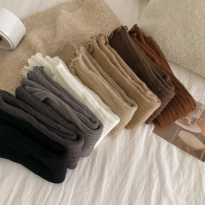 Cozy knit leg warmers in various colors with ruffle cuffs on a soft white bed sheet