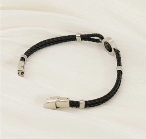 Detail of black braided leather bracelet with silver anchor star charm on white silk background