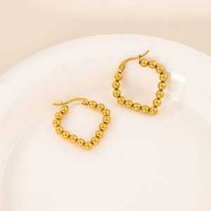 Polished gold beaded hoop earrings displayed on a minimalist white ceramic tray