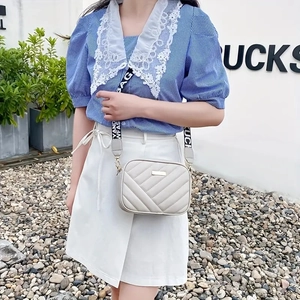 Detail of embroidered crossbody camera bag with V-quilted pattern and wide woven strap