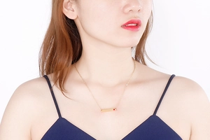 Close-up of golden horizontal bar necklace with a tiny red gemstone on model's neckline