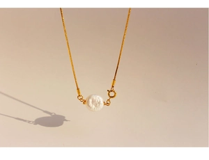Close-up of golden snake chain with a natural baroque pearl pendant on beige background