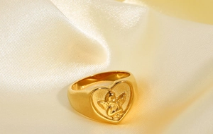 Macro shot of 18k gold-plated stainless steel angel relief ring on beige silk background