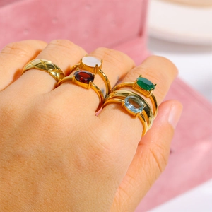 Close-up of stacked gold rings with colorful gemstones worn on a model's hand