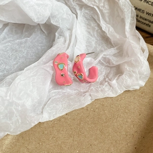 Detail view of pink C-shaped heart earrings with blue oil drip and crystals on gold alloy