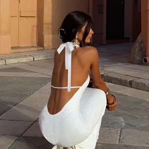 Detail of a backless halter white dress featuring a tied bow and textured fabric on a woman