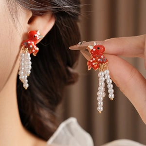 Detail of vintage red enamel ox earrings with elegant white pearl tassel drops