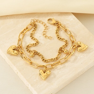 Nahaufnahme des goldfarbenen Doppelarmbands mit Herzanhängern auf Marmor
