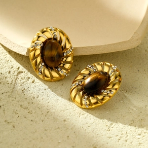 Vintage gold oval earrings with tiger eye stone and crystal accents on stone surface