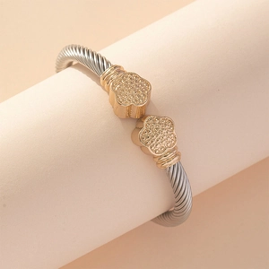 Two-tone stainless steel cable wire cuff bracelet with gold floral ends on a stand