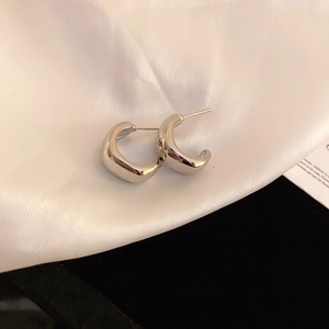 Close-up of silver minimalist C-shaped metal hoop earrings on elegant silk background