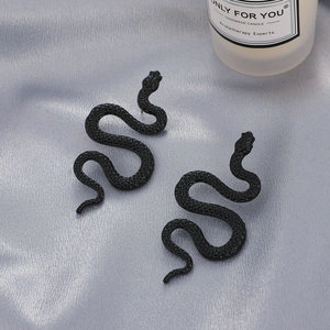 Matte black snake earrings with scale texture on gray silk fabric and candle background