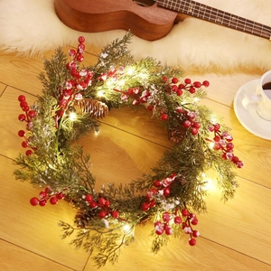 Christmas wreath with green needles, red berries, pine cones and warm LED lights
