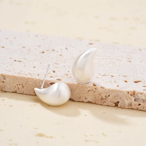Minimalist matte silver teardrop earrings on textured stone base for a premium aesthetic