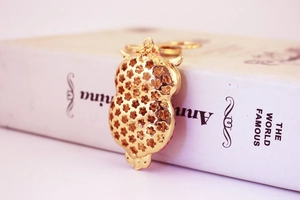 Close-up of golden owl metal keychain with intricate hollowed flower pattern on the back