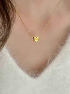 Close-up of a polished gold heart pendant necklace on a soft white knit sweater