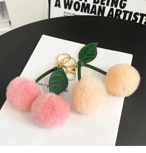 Close-up of pink and beige cherry plush keychains with green leather leaves and gold ring