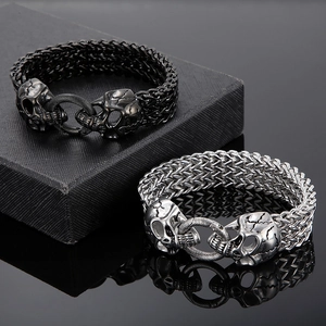 Close-up of black and silver stainless steel skull bracelets on a textured jewelry box