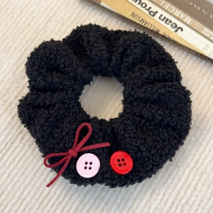 Détail du chouchou en peluche noire avec nœud rouge et boutons décoratifs sur fond beige