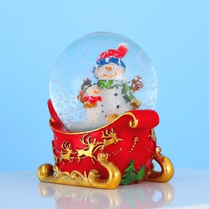 Christmas snow globe with cute snowmen on a red sleigh base featuring golden reindeer