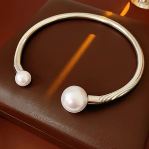Close-up of a silver open choker necklace with pearls on a dark leather display