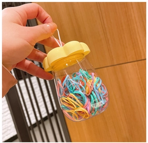 Close-up of a clear jar with a yellow flower lid containing colorful hair ties for kids