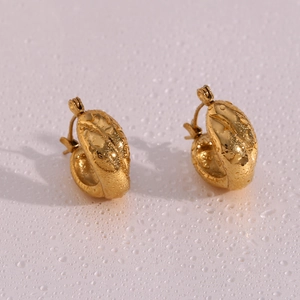Macro view of gold plated croissant dome earrings resting on a surface with water droplets