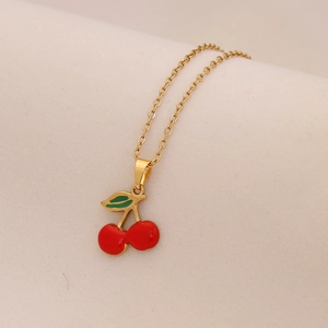 Primo piano di una collana a catena dorata con ciondolo a ciliegia rossa e foglia verde