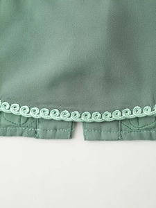 Gros plan sur les broderies florales vertes et la texture du tissu de cet ensemble de vacances