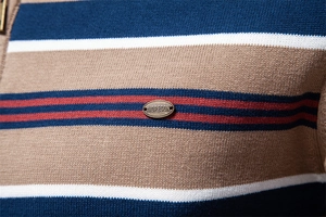 Detail of striped knit sweater fabric with metal logo and half-zip texture