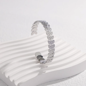 Detalle del brazalete abierto de acero inoxidable plateado con diseño de hojas