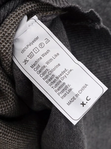 Close-up of gray knit cardigan fabric showing the 100% polyester care label and texture