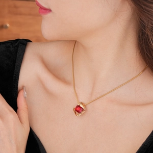 Close-up of a gold necklace featuring a square red gemstone pendant on a model's neck