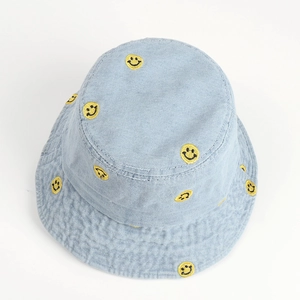 Detail of yellow smiley face embroidery on light blue denim fabric fisherman bucket hat