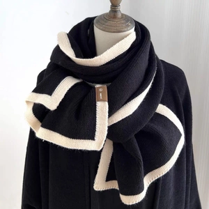Elegant black knit scarf with white border on mannequin, featuring a brown logo patch