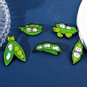 Detailed set of five creative pea pod cat enamel pins displayed on blue fabric background