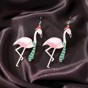 Detail of acrylic pink flamingo earrings with Christmas hat and scarf on silk fabric
