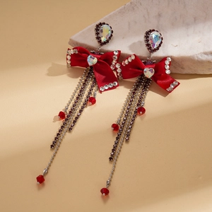 Macro detail of red bow earrings with long rhinestone tassels on a marble prop