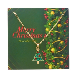 Detail of gold necklace with green Christmas tree pendant on Merry Christmas card background