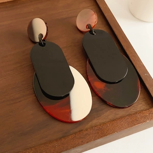 Close-up of mismatched geometric acrylic earrings with amber and mahogany resin pendants