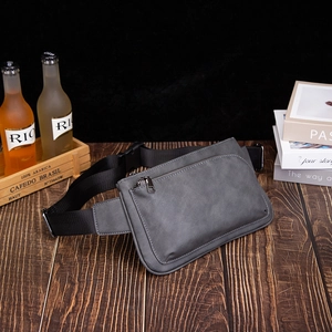 Minimalist matte grey sling bag with adjustable strap and front zip pocket on a wooden desk