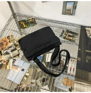 Detail of minimalist black nylon crossbody bag on a metal mesh shelf with aesthetic cards