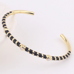 Detail of gold open bracelet with black enamel segments and white circular accents