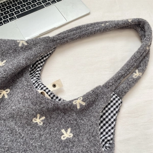 Detailed view of gray knitted tote bag with bow embroidery and black plaid lining detail