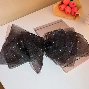 Grande pince à cheveux élégante en organza noir avec paillettes posée sur un livre