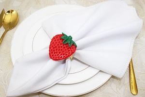 Detailed view of a red strawberry napkin ring with metal band on a white cloth napkin